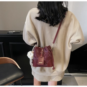 Burgundy bucket bag with polka dot texture and plush charm on female model shoulder