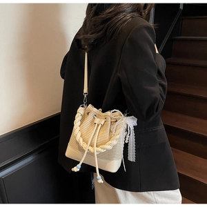 Detail of cream woven bucket bag with leather base, drawstring, and pearl bow charm
