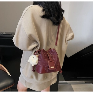 Detail of wine red bucket bag with snake skin texture and white fluffy ball pendant
