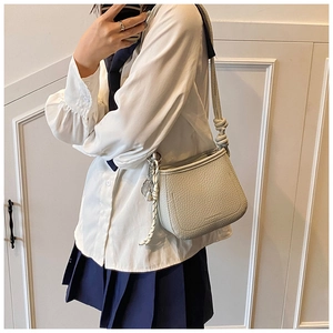 Close-up of beige lychee leather crossbody bag with knot strap and metallic charm