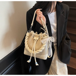 Close-up of woven bucket bag with pearl pendant, lace bow and drawstring closure