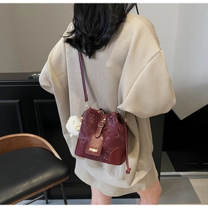 Detail view of burgundy bucket bag with python texture and white faux fur pompom