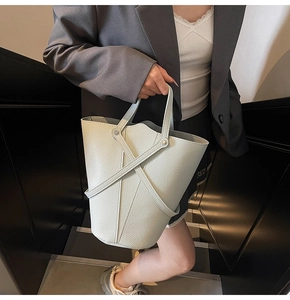 Detail of light gray bucket bag with cross strap design and litchi grain leather texture