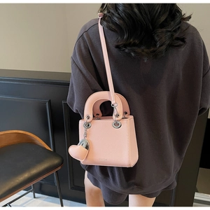 Detail shot of a pink pebbled leather handbag with heart charm on a model