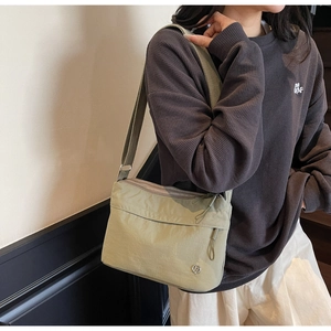 Detail view of light green nylon crossbody bag with multiple zippers worn by a model