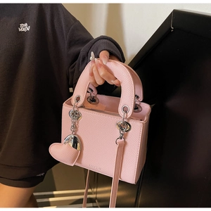 Detail of pink lychee leather bag featuring round handles and heart-shaped pendant charm