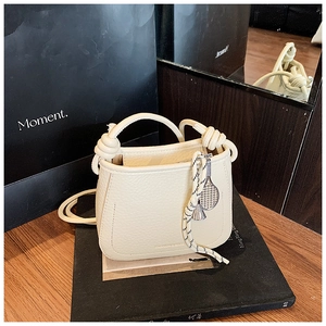 Close-up of cream bucket bag with litchi texture, knot handles and tennis racket charm