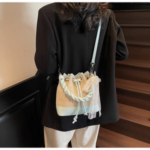 Detail of woven bucket bag with blue leather trim and delicate lace charm decoration