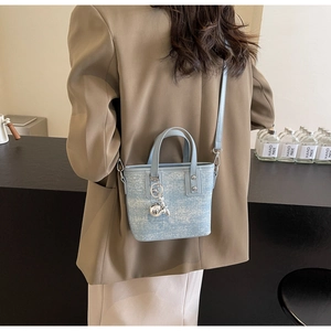 Close-up of a light blue textured bucket bag with silver charm on a female model