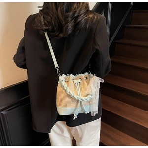 Detail of straw bucket bag with blue leather trim and delicate lace decor on strap