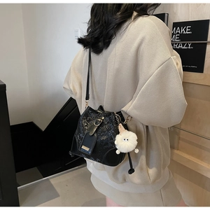 Detail of black snakeskin bucket bag featuring a white plush monster charm with big eyes