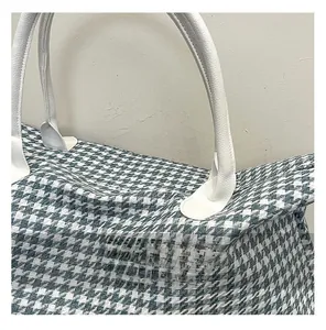 Detailed view of green houndstooth travel bag with white leather handle and stitching