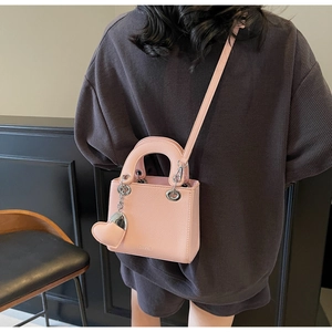 Detail of pink mini handbag with lychee texture and heart charm shown on model