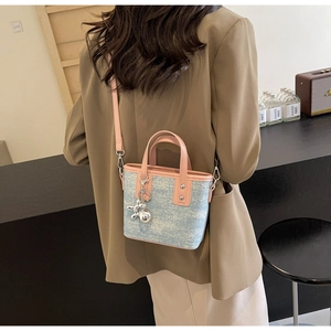 Detail of light blue denim bucket bag with pink leather trim and metallic dog charm