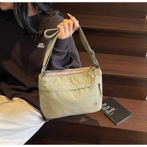 Close-up of light green nylon crossbody bag with multi-layer zippers and silver logo
