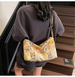 Close-up of beige crossbody bag with embroidered bear and floral patterns