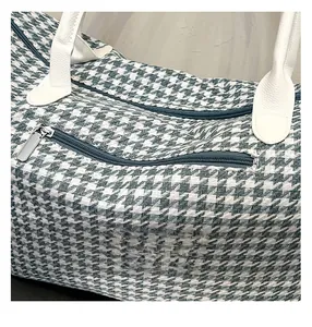 Close-up of houndstooth travel bag showing blue zipper and white leather handle detail