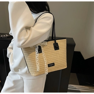 Détail du sac cabas en paille tressée avec anses noires et nœud en dentelle blanche