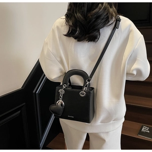 Detail of black litchi grain leather crossbody bag with heart charm and silver hardware