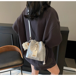 Detail of silver bucket bag with scale texture and plush sheep charm on crossbody strap