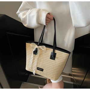 Détail du cabas en paille tissée avec poignées en cuir noir et nœud en dentelle blanche