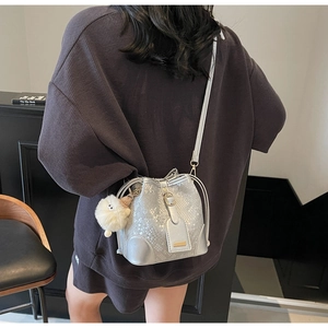 Detail of silver bucket bag with snake skin texture and white plush ball accessory