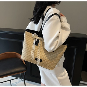 Détail du sac cabas en paille tressée avec anses en cuir noir et nœud en dentelle blanche