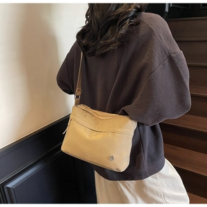 Close-up of a beige canvas crossbody bag with adjustable strap worn by a female model