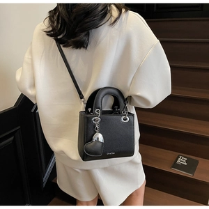 Detail of black lychee leather handbag featuring silver hardware and heart-shaped charm