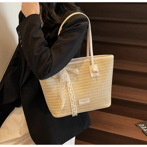 Détail du sac cabas en paille tissée avec poignées en cuir blanc et nœud en dentelle