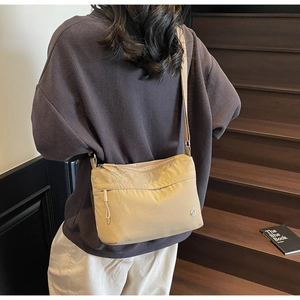 Detail of beige nylon crossbody bag with zipper pockets and wide fabric strap shown on model