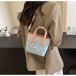 Detail of blue denim crossbody bucket bag with pink handles and silver dog charm