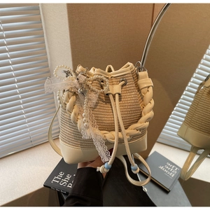 Detailed close-up of woven bucket bag with pearl strap, lace details and heart pendant