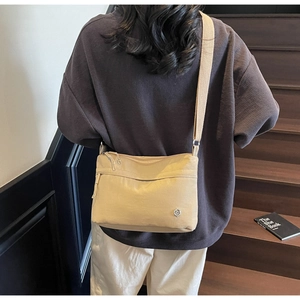 Detail of beige nylon crossbody bag with multiple zippers and adjustable fabric shoulder strap