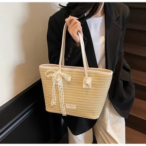 Détail du sac cabas en paille avec un nœud en dentelle blanche et des anses en cuir