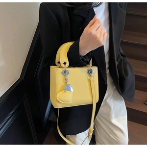 Detail of yellow lychee leather handbag with heart pendant and silver chain strap