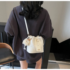 Detailed side view of white faux leather bucket bag with crocodile texture and plush charm