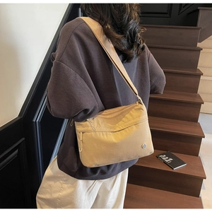 Model wearing a khaki nylon crossbody tote with multi-zipper pockets and wide shoulder strap