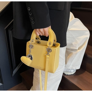 Detail of yellow pebbled leather handbag with heart charm and adjustable strap held by a model