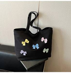 Detail of black canvas tote bag featuring colorful polka dot bows on a leather sofa