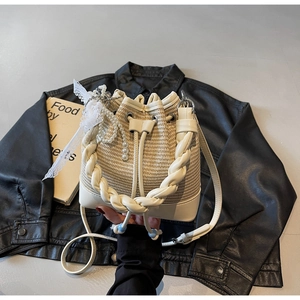 Detail of cream woven bucket bag with pearl pendant and lace charm on black jacket