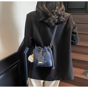 Detail of dark blue faux python skin bucket bag with gold clasp and white fluffy charm
