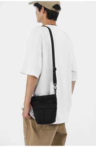 Dettaglio di una borsa a tracolla da uomo in nylon nero con etichetta arancione di marca