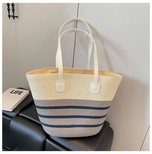 Detalle del bolso tipo tote de paja tejida con rayas azules y asas de cuero blanco