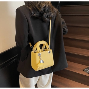 Yellow pebble leather mini handbag worn with a black suit on wooden stairs