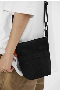 Dettaglio della borsa a tracolla nera minimalista in nylon con etichetta arancione