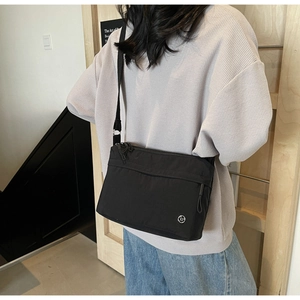 Detail of a black minimalist nylon crossbody bag with silver logo worn by a model