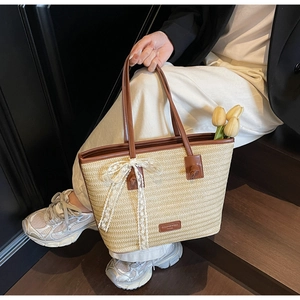 Détail du sac cabas en paille tressée avec nœud en dentelle blanche et anses en cuir