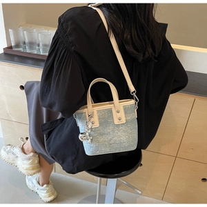 Detail of light blue denim bucket bag with leather handles and metallic rabbit charm