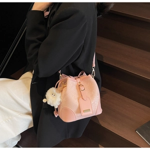 Pink snakeskin bucket bag with plush charm shown on a shoulder strap for daily commuting
